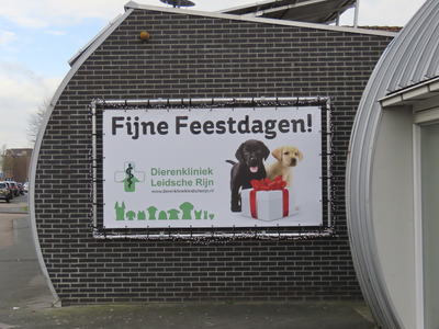 902169 Afbeelding van het spandoek 'Fijne Feestdagen!' met twee hondenpups, op de zijgevel van Dierenkliniek Leidsche ...